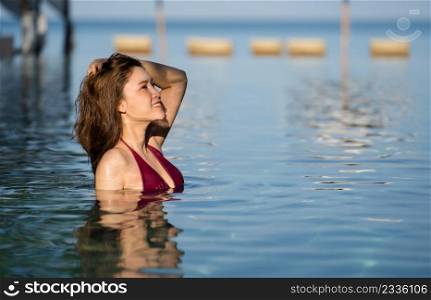 young woman in swimsuit relaxing in swimming pool with sea background