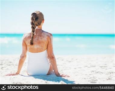 Young woman in swimsuit sitting on sandy beach . rear view