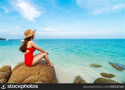 young woman in swimsuit sitting on stone beach with sea at Koh MunNork Island, Rayong, Thailand