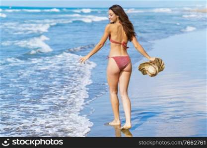 Young woman in swimwear and sunhat, enjoying the beach on her holiday.. Woman in swimwear and sunhat, enjoying the beach on her holiday.