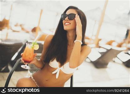 Young woman in swimwear drinking cocktail on the beach