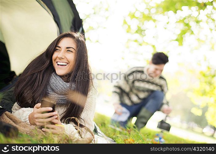 Young woman in tent using smartphone, laughing