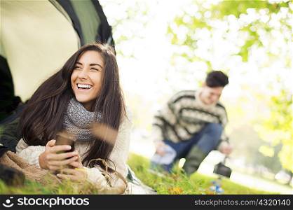 Young woman in tent using smartphone, laughing