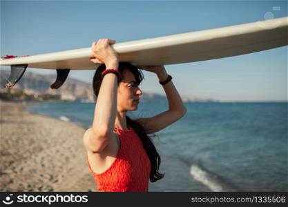 Young woman in the beach with her surfboard over her head