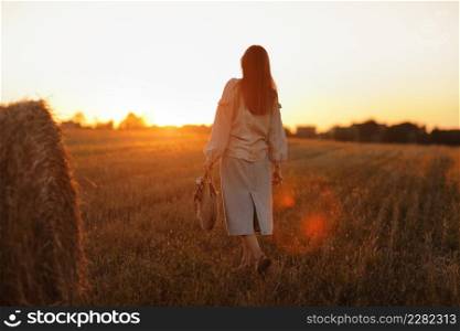 young woman in the beautiful light of the summer sunset in a field is walking near the straw bales. beautiful romantic girl with long hair outdoors in field. young woman in the beautiful light of the summer sunset in a field is walking near the straw bales. beautiful romantic girl with long hair outdoors in field.