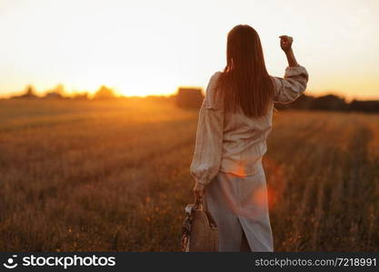 young woman in the beautiful light of the summer sunset in a field is walking near the straw bales. beautiful romantic girl with long hair outdoors in field. young woman in the beautiful light of the summer sunset in a field is walking near the straw bales. beautiful romantic girl with long hair outdoors in field.