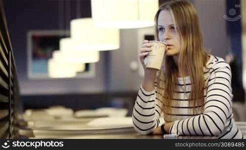 Young woman in the cafe drinking tea and looking at her watch waiting for somebody