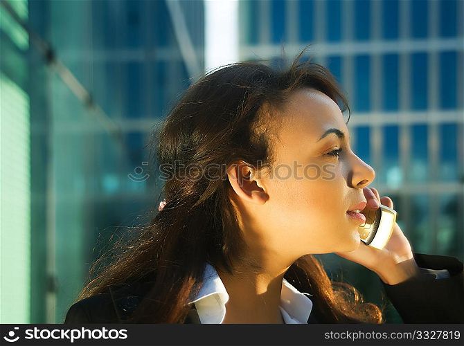 Young woman in the evening sun using her cellphone in front of a modern glass and steel building