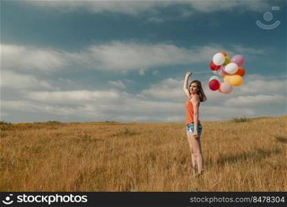 Young woman in the field holding colorful balloons