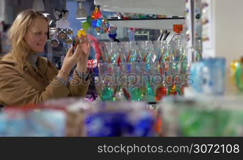 Young woman in the shop of Venetian glass. She examining different glasses decorated with colorful ornate patterns