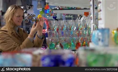 Young woman in the shop of Venetian glass. She examining different glasses decorated with colorful ornate patterns