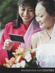 Young woman in the wedding dress looking at a photograph with another woman