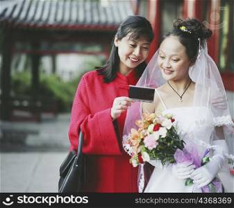 Young woman in the wedding dress looking at a photograph with another woman