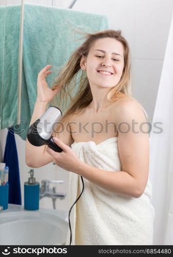 Young woman in towel drying hair at bathroom