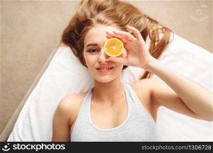 Young woman in underwear lies in bed and looks through a slice of lemon. Girl wake up in the morning in bedroom