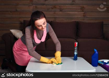 Young woman in uniform and rubber gloves cleans the table. Cleaning servisce concept. Woman in uniform and rubber gloves cleans table