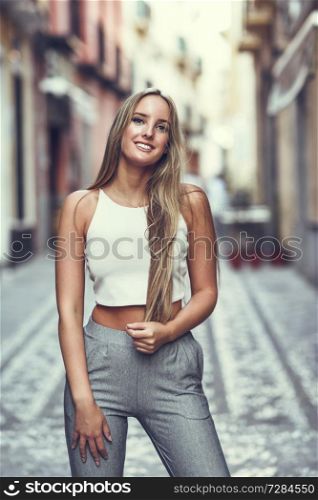 Young woman in urban background. Blond girl with straight hairstyle wearing casual clothes in the street.