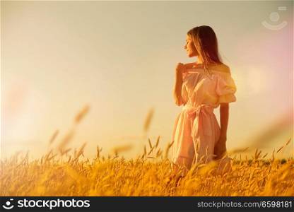 Young woman in wheat field at sunset