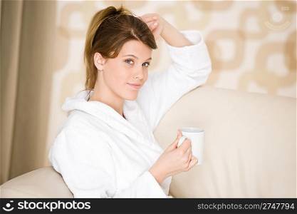 Young woman in white bathrobe with coffee in lounge