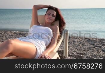 Young woman in white short dress resting by the sea