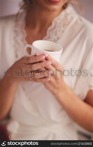Young woman in white silk robe with white cup of beverage tea or coffee in the morning.. Young woman in white silk robe with white cup of beverage tea or coffee in the morning