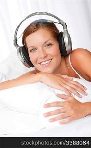 Young woman in white with headphones listening to music in bed