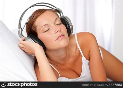 Young woman in white with headphones listening to music in bedroom