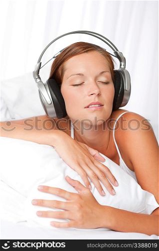 Young woman in white with headphones listening to music in bedroom