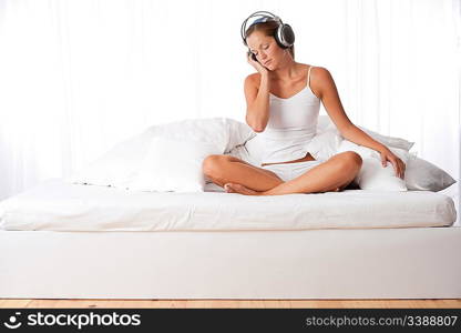 Young woman in white with headphones listening to music in bedroom