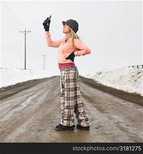Young woman in winter clothes standing on muddy dirt road looking at cell phone.