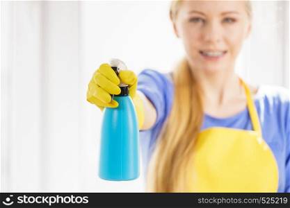 Young woman in yellow gloves cleaning window pane at home with spray detergent. Cleaning concept. Woman cleaning window at home
