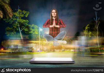 Young woman in yoga pose hovers above a big phone with a glowing screen, evening street with long exposure light effect on background. Communication god. Evening street