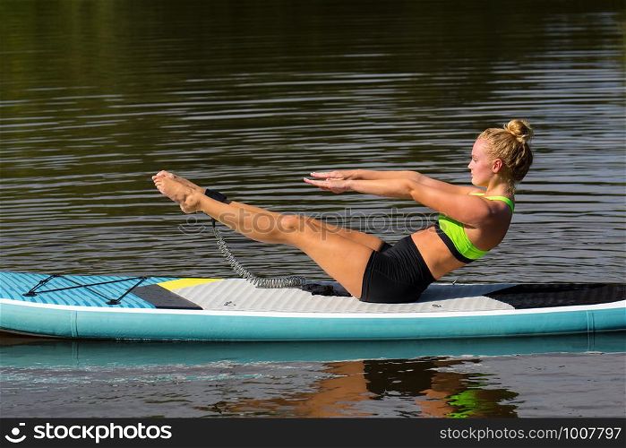 Young woman in yoga posture on SUP on water surface