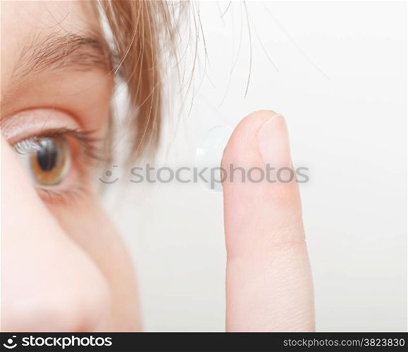 young woman inserts contact lens in eye close up