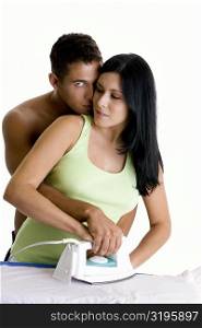 Young woman ironing with a young man embracing her from behind