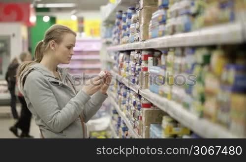 Young woman is choosing food for her child in the shopping center. No visible trademarks or logos. Middle shot with shoppers in background.