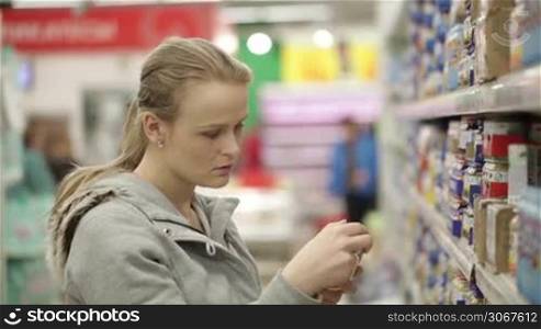 Young woman is choosing food for her child in the supermarket.