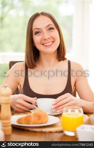 Young woman is drinking a hot cup of coffee while having a breakfast at home