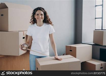 Young woman is loading and packing boxes for moving. European lady is wrapping cardboard boxes with packing tape. Moving service worker preparing boxes for shipping and storage. Delivery service.. European lady is wrapping cardboard boxes with packing tape. Moving service worker.