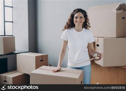 Young woman is loading and packing boxes for moving. European lady is wrapping cardboard boxes with packing tape. Moving service worker preparing boxes for shipping and storage. Delivery service.. European lady is wrapping cardboard boxes with packing tape. Moving service worker.