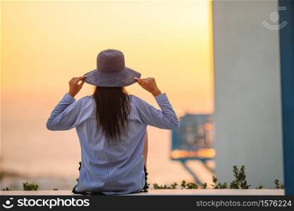 Young woman is looking at the sunset over a sea in famous village Mykonos with the old buildings in the background. Soft summer backlight.. Young woman is looking at the sunset over a sea in famous village Mykonos