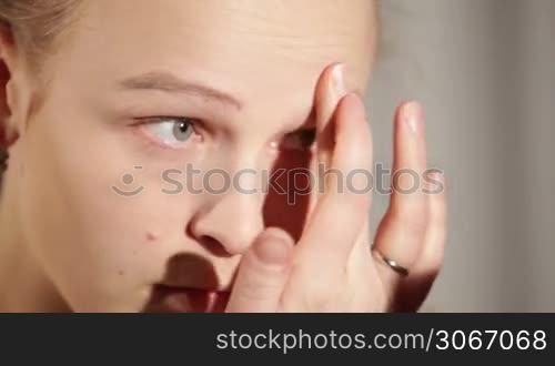 Young woman is putting cosmetic cream on her face. Close up.