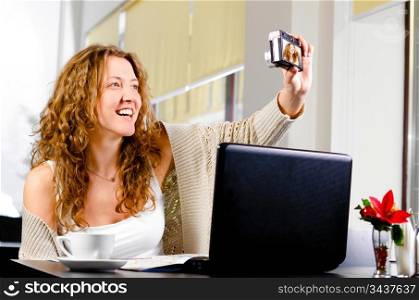 young woman is sitting at cafe and taking a picture of herself