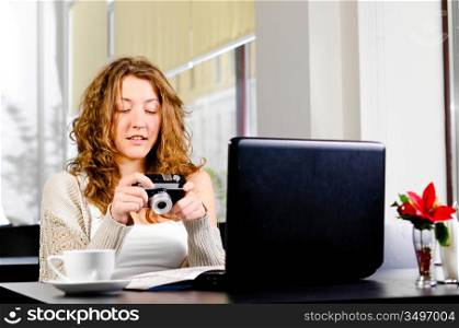 young woman is sitting at cafe and watching photos on her camera