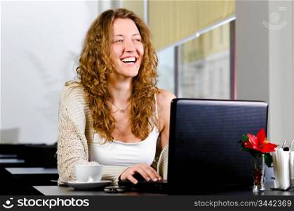 young woman is sitting at cafe and working on laptop