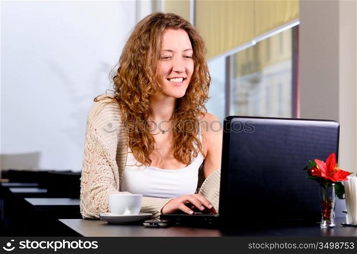 young woman is sitting at cafe and working on laptop