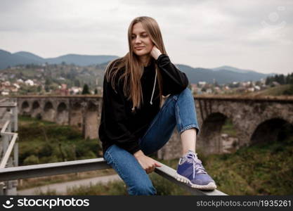 Young woman is sitting near old viaduct. Tourist girl in scenery countryside by the Historical abandoned railway arch bridge viaduct in Vorokhta, Ivano-Frankivsk Region, Ukraine.. Young woman is sitting near old viaduct. Tourist girl in scenery countryside by the Historical abandoned railway arch bridge viaduct in Vorokhta, Ivano-Frankivsk Region, Ukraine