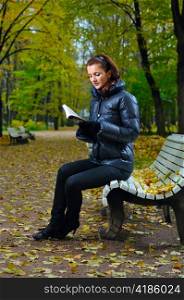 young woman is sitting on a bench in an autumn park and reading