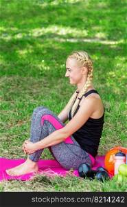 Young woman is sitting on a roll mat wearing sportswear in the public park.. Young woman sitting in the public park.