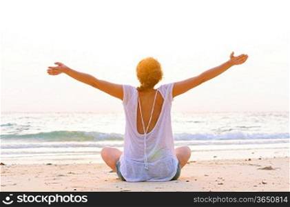 young woman is sitting on beach at sunrise